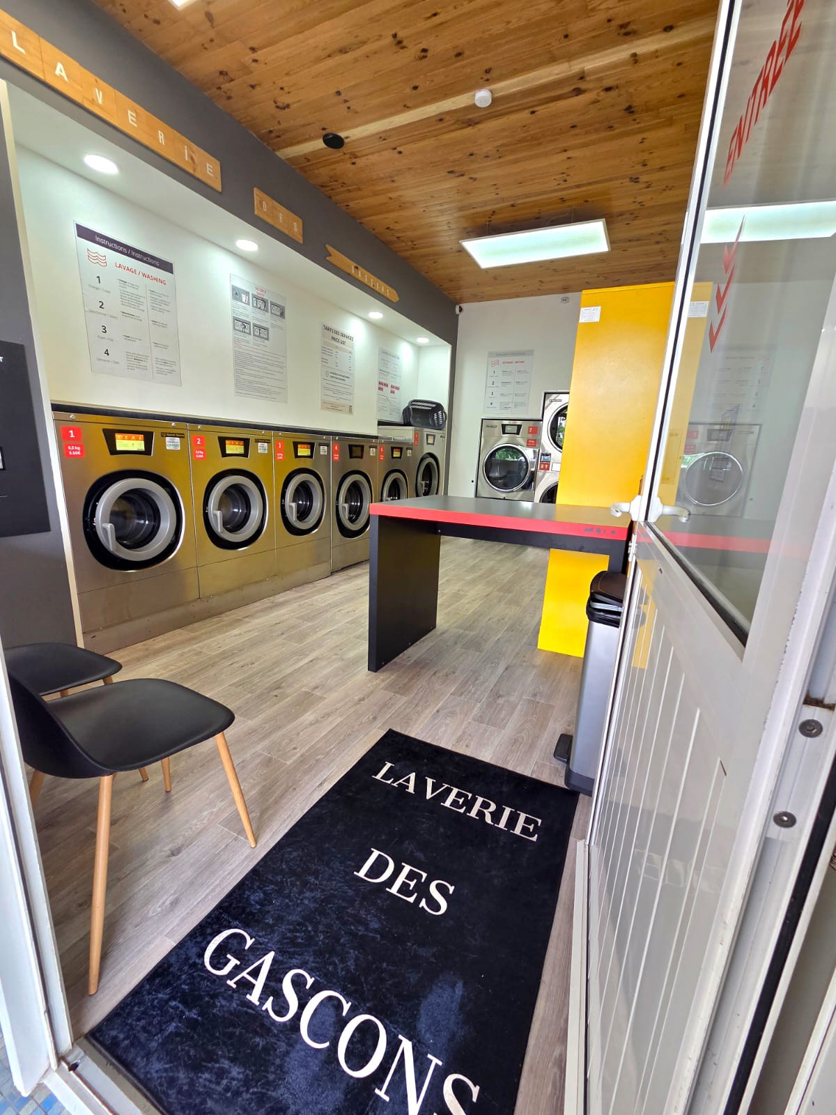 Entrée de la laverie — tapis à l’enseigne et lave-linge professionnels