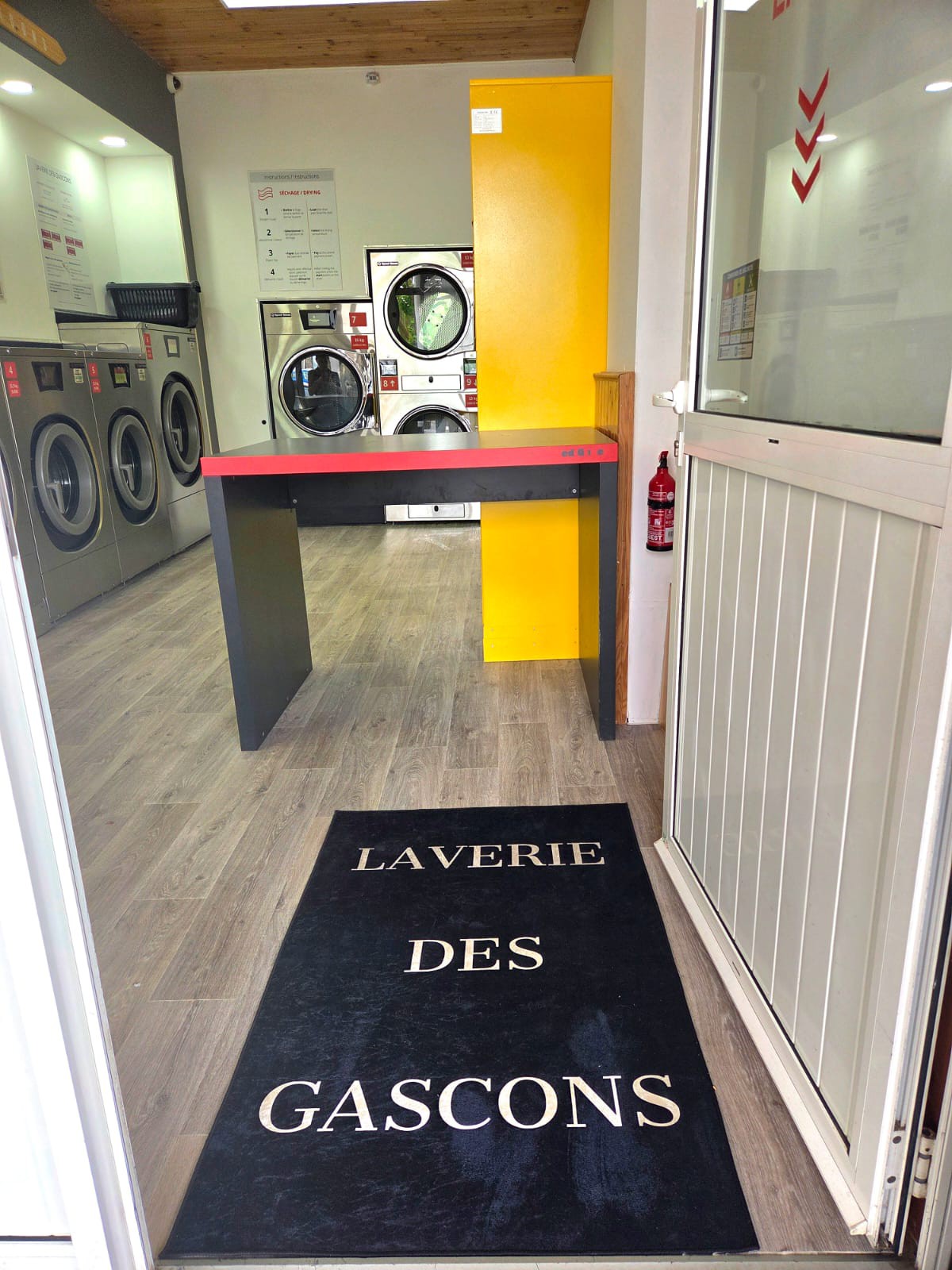 Entrée principale avec tapis Laverie Des Gascons et extincteur de sécurité