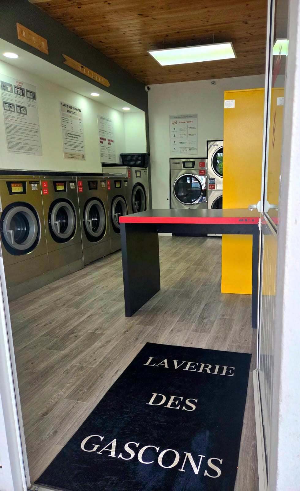Vue latérale — rangée de machines à laver et panneaux d’instructions